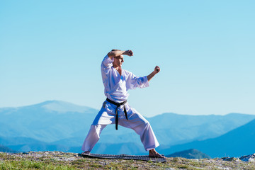 Blond karate athlete does kata on top of a mountain while performing a line up of kicks, punches and blocks on top of a mountain on a sunny day. © qunica.com