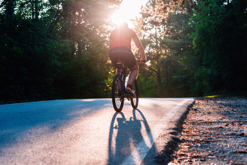 Male cyclist riding his bike on sunset on a road through deep woods. Extreme biker no safety equipment.