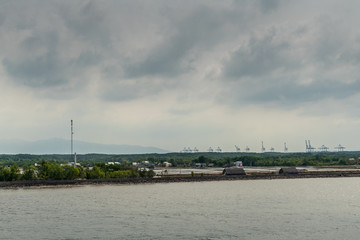 Long Tau River, Vietnam - March 12, 2019: At Thieng Lieng just up from mouth of river: International Container Terminal of Tan Cang visible behind water treatment plant under dark cloudscape.