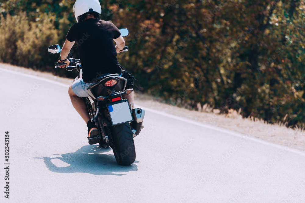 Wall mural driver riding motorcycle on an asphalt road through forest