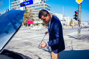 A handsome businessman wearing blue blazer lifting up the hood of his car and checking the oil...