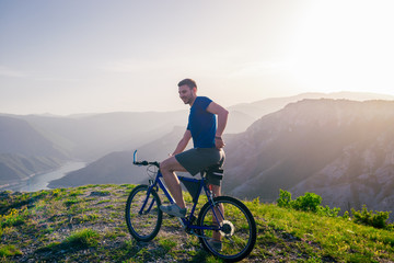 Fototapeta premium Adventurous Cyclist riding his mountain bike at the edge of a cliff, on rocky terrain while wearing no safety equipment.Amazing top view.