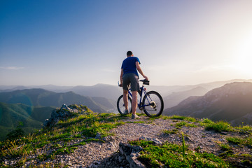 Adventurous Cyclist riding his mountain bike at the edge of a cliff, on rocky terrain while wearing...