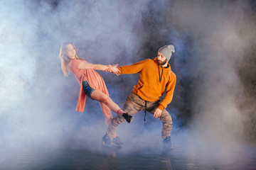 Couple dancing modern dance and showing off their leg stretch moves.Black background while the couple is dressed in urban colorful clothes...