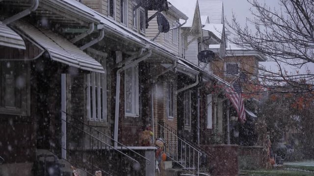 A snowy view of typical middle class row houses in a small town's residential neighborhood. American flag on a porch. Pittsburgh suburbs. Shot in slow motion.  	