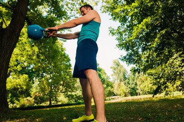 Handsome man lifting kettlebell in th park