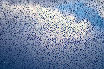 Sky and clouds reflected in glossy surface with rain drops.