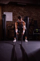 Fototapeta na wymiar Muscular man is doing battle rope exercise
