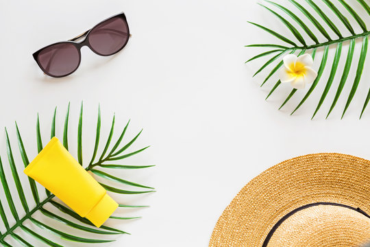 Top view of suncream, straw hat, palm leaf, sunglasses. spf cream on white background with copy space. Directly above. Bright summer, vacations, skincare concept. Flat lay, template, mockup