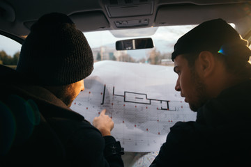 Two robbers planning and pointing on the blueprint(map) their objective while holding their guns.
