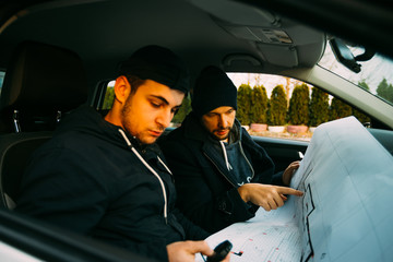 Two armed bandits sitting in a car planning their next robbery, while counting on a stopwatch the...