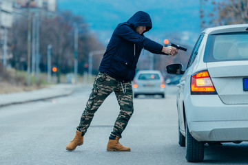 Gangster with a gun trying to rob a guy which is sitting in his car.