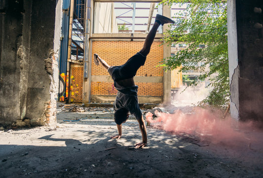 Young man doing parkour handstand around colored smoke bomb - Powered by Adobe