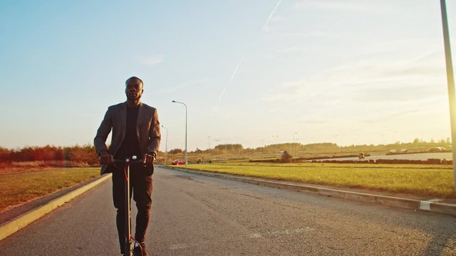 Cheerful young black businessman riding on electric scooter enjoying travel in picturesque countryside outdoor. Sunset time. Modern green transport. Ecology.