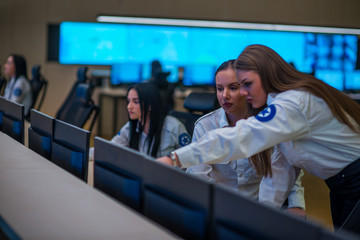 Obraz premium Security guard monitoring modern CCTV cameras in a surveillance room. Female security guards sitting having conversation monitoring cctv.