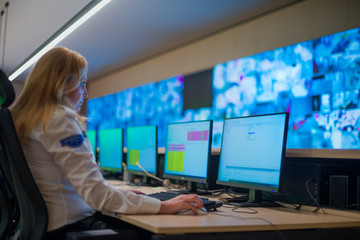 Female security guard sitting and monitoring modern CCTV cameras in a surveillance room.
