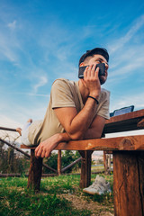 Freelancer man talking on mobile while lying on wooden table in nature
