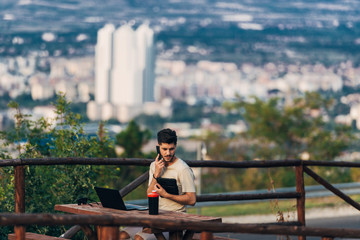 Freelancer man working on laptop while sitting on wooden table in nature