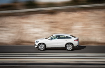 Fototapeta na wymiar White car moving fast along the street on a motion blurred background. Car driving on freeway, motion blur. Luxury-car.