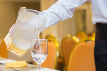 The waiter is pouring water into the glass  on the restaurant table
