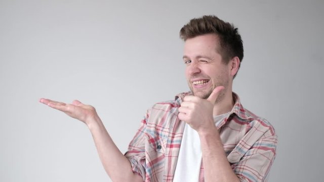 Young man smiling and pointing aside reccomending to buy something.