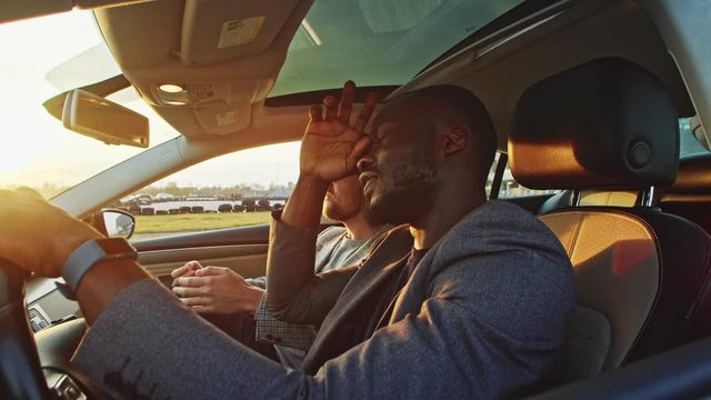 Upset young african businessman having trouble with car sitting inside vehicle with friend or colleague frustrating in despair. Car failure. Unsatisfaction.