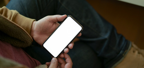 Close-up view of young male freelancer using his blank screen smartphone in comfortable workplace