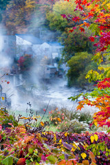 Shiroi River hot springs steaming in early frosty Autumn morning framed by colorful leaves. Jozankeionsenhigashi, Hokkaido, Japan