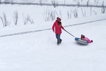 Active young mother rolls her baby on a snow tubing. Winter activities. Happiness to be a parent. Family look. 