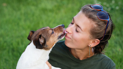 Dog kissing her owner outside. Lovely woman walking with her Jack Russell Terrier in summer landscape. Having fun playing in outdoors. Playful mood. Enjoying freedom. Friendship, pets, togetherness