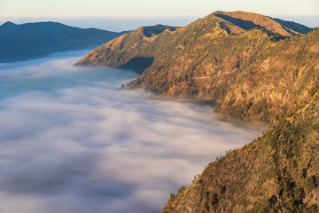 Clouds covering the "Sea of Sands" around Mount Bromo, East Java, Indonesia, pushing against the steep hills surrounding the plain. 