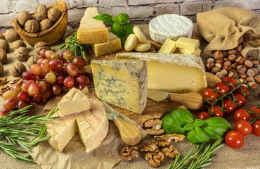 Assortment of cheeses with  herbs, vegetables, nuts and grapes. Food for wine, cheese delicatessen on a wooden board.
