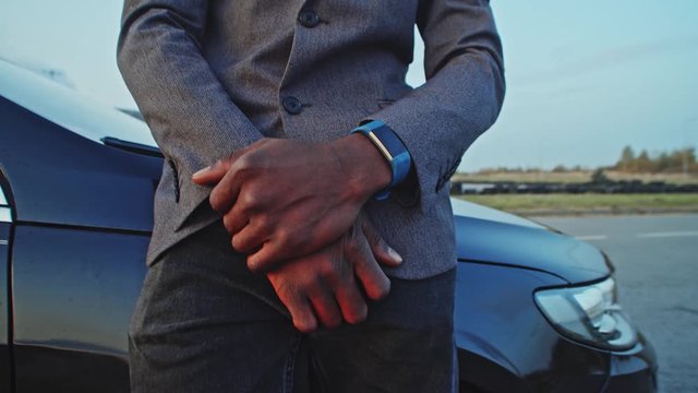 Close-up attractive black young man in business attire leaning on car hood staying outdoors. Portrait confident handsome african entrepreneur at modern cityscape.
