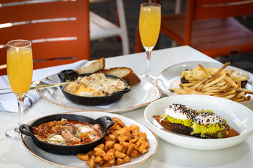 Business lunch of  jamon and ham skillet, toast with avocado and egg, grilled beef with french fries and pan with brussels sprouts with drinks outside a restaurant in a sunny day 