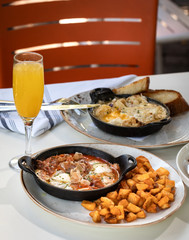 Business lunch of  jamon and ham skillet, toast with avocado and egg, grilled beef with french fries and pan with brussels sprouts with drinks outside a restaurant in a sunny day 