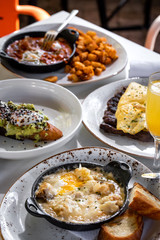 Business lunch of  jamon and ham skillet, toast with avocado and egg, grilled beef with french fries and pan with brussels sprouts with drinks outside a restaurant in a sunny day 