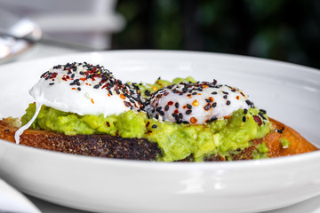 Haute cuisine - grilled sandwich with avocado guacamole sauce and two sunny side up eggs outside restaurant in a sunny day