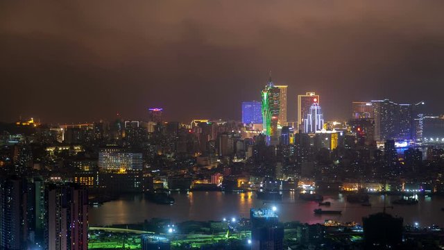 Timelapse illuminated Cathedral Parish near various flashing buildings and skyscrapers of Macau Peninsula and sailing boats at night in China