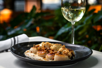 Haute cuisine - grilled king shrimps with white sauce on black dish in outdoors restaurant with glass of white wine