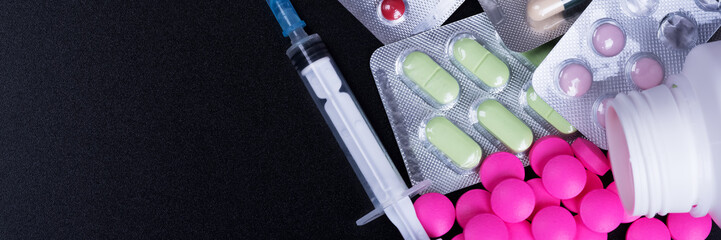 Colorful pills, blister and syringe on a black background.