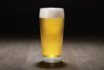 A glass of Pale Ale, lager, pilsner draft beer on wooden surface and black background