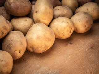 Rustic potatoes. Vegetables from farmhouse field is lying in bulk on wooden table from planks. Place for your text in one corner of picture.