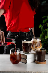 Female barista pouring cherry juice into iced black coffee
