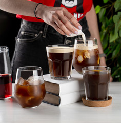 Female barista pouring milk into a glass of iced coffee with swirl and splash