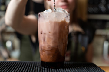 Bartender is making milky alcoholic cocktail pouring and stirring cream into the glass