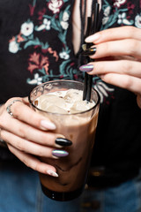 Woman is holding a glass of vanilla iced latte in hands with beautiful manicure