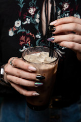Woman is holding a glass of vanilla iced latte in hands with beautiful manicure