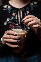Woman is holding a glass of vanilla iced latte in hands with beautiful manicure