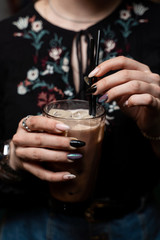 Woman is holding a glass of vanilla iced latte in hands with beautiful manicure