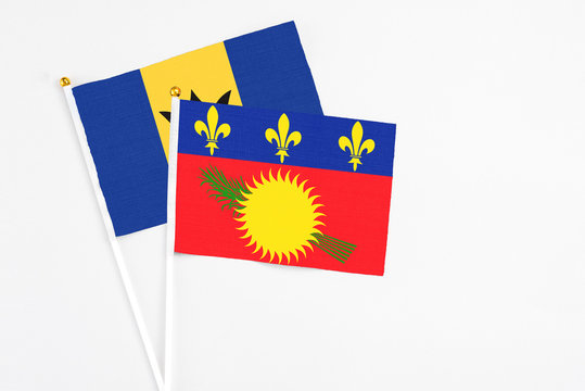 Guadeloupe and Barbados stick flags on white background. High quality fabric, miniature national flag. Peaceful global concept.White floor for copy space.